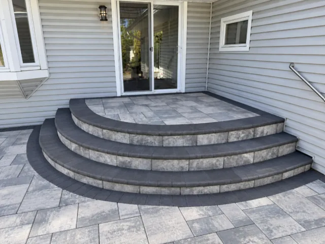 Curved gray paver steps with dark edges below a sliding glass door.