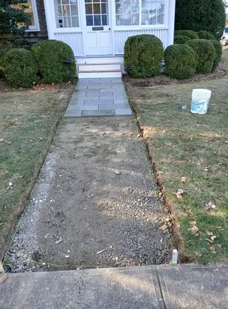 Rectangular stone front walkway partway through installation beside an exposed prepared route.