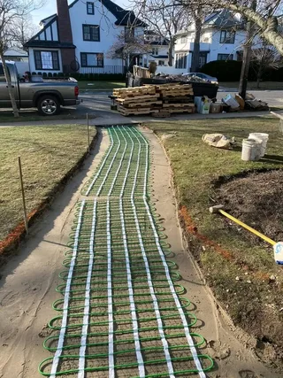 Heating tubing laid along a curved front walkway base before paving installation.