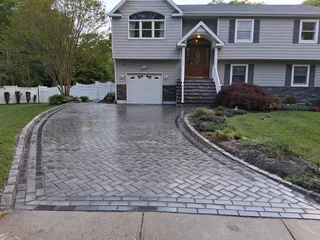 Curved herringbone paver driveway with a dark border in front of a gray house.