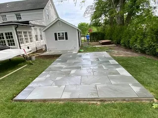 Large-format gray patio paving beside a house and lawn.