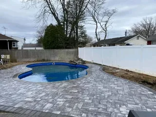 Kidney-shaped pool with gray paver paving and a curved coping edge.
