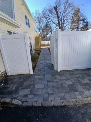 Finished gray paver side path between a house and white fencing.